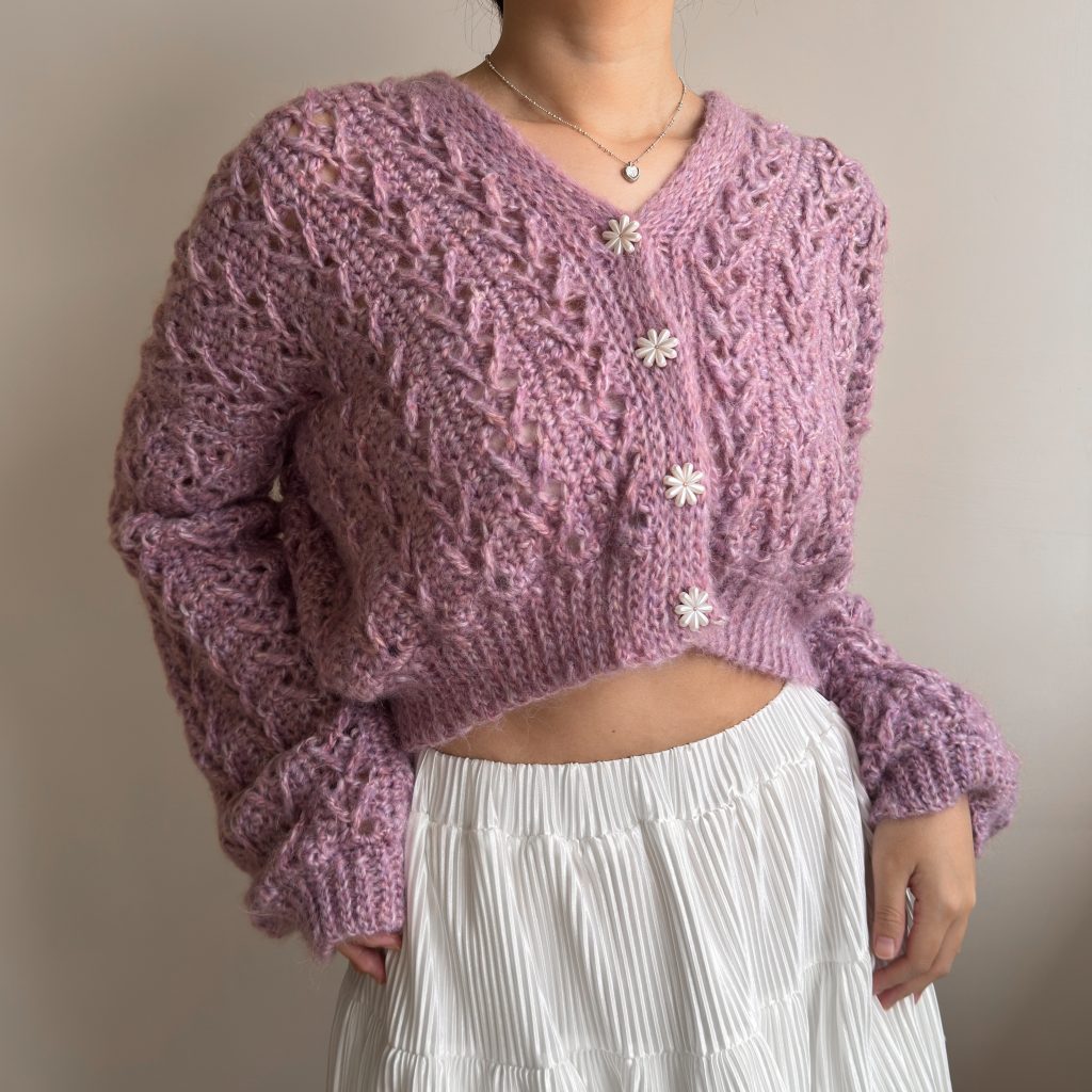Close-up of a mauve Fiia crochet cardigan with textured openwork stitches, ribbed edging and flower buttons.