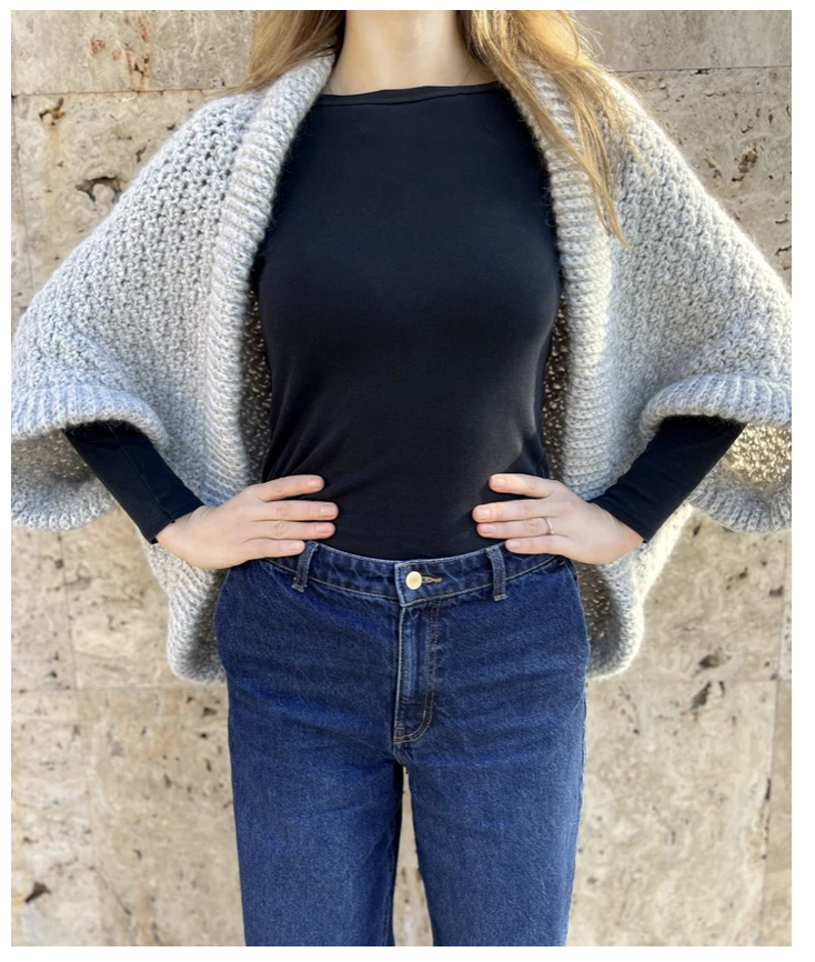 Woman wearing a light grey Eloween Cocoon crochet cardigan with an oversized draped shape and ribbed edging.