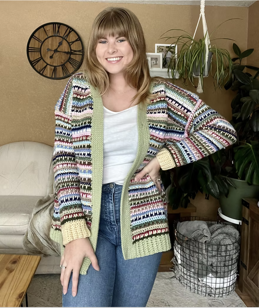 Woman wearing a colourful striped Ultimate Stash-Buster crochet cardigan with pale green edging and cream cuffs.